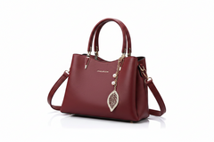 Red leather tote-style handbag with top handles, side strap, gold hardware, leaf charm