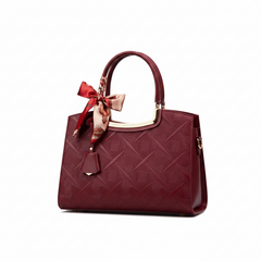 Wine red embossed leather handbag with top handle, bow charm, and gold-toned trim
